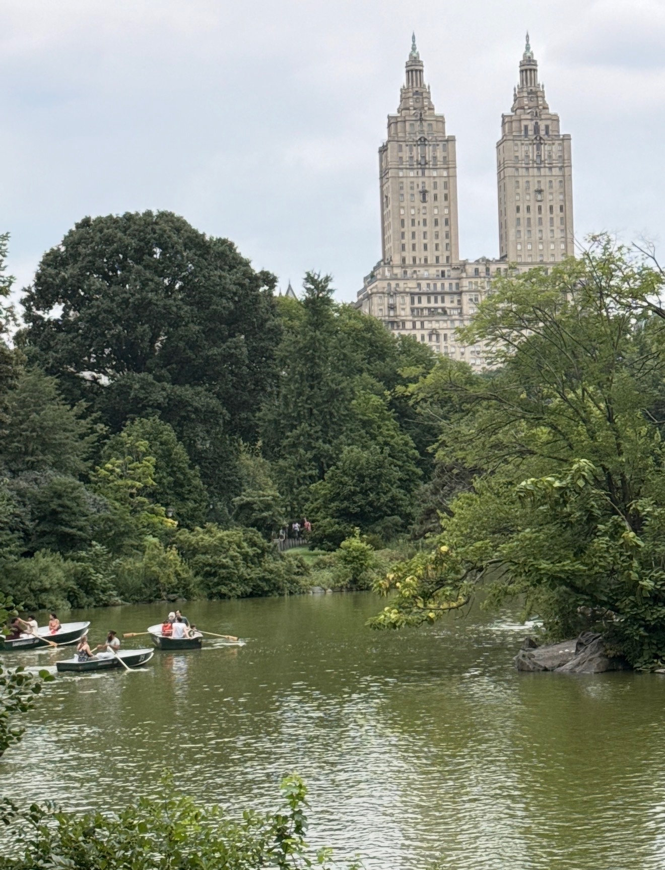 Rowboats on the lake in Central Park with the twin towers of the San Remo rising behind the trees